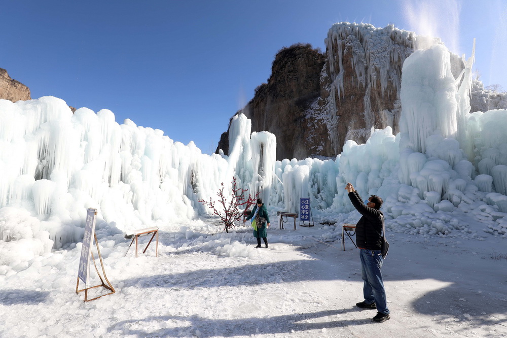 12月16日,在河北省平山县沕沕水景区,游客在冰瀑中拍照游玩。