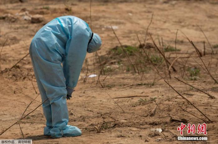 资料图：印度新德里的墓地里，在埋葬死于新冠病毒的中央后备警察部队(CRPF)工作人员前，一名医护人员弯下了腰。